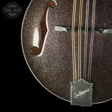 Close-up of a Gibson electric guitar body showing the glittering dark brown finish, f-holes, strings, and a silver Gibson tailpiece against a black background.