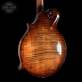 Close-up of the back of a mandolin with a glossy, highly figured brown wood finish, set against a solid black background. A Tone Shop watermark is visible in the top-left corner.