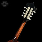 Close-up of the headstock of a wooden stringed instrument, likely a mandolin or small guitar, featuring a glossy brown flamed wood neck, black headstock, ornate silver tuning pegs, and white tuning keys against a solid black background.