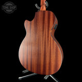 Wooden acoustic guitar on a stand with 'Tone Shop' logo in the corner.