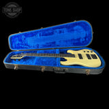 Cream-colored bass guitar in a blue-lined case with 'Tone Shop' logo.