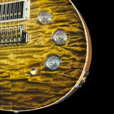 Close-up of a gold-finish electric guitar body with a flamed maple wood pattern, chrome hardware, and clear control knobs against a black background.