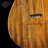 Close-up of a wooden electric guitar body showing the natural wood grain finish, pickguard, and part of the bridge against a black background. A Tone Shop watermark is visible in the top left corner.