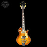 A Les Paul Custom electric guitar with a natural flame maple top, shown against a solid black background. The guitar features a black headstock with gold tuning pegs and a black neck with maple block inlays.
