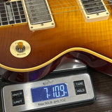 Close-up of a sunburst electric guitar body resting on a digital scale showing 7.109 oz, with the scale brand Wristlet visible.