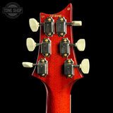 Close-up of a red electric guitar's headstock with tuning pegs on a black background.
