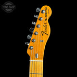 Close-up of a Fender Telecaster electric guitar headstock in a natural wood finish, showing six tuning pegs and the Fender logo, set against a solid black background.