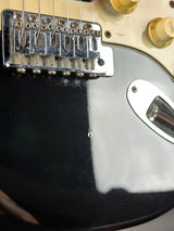 Close-up of a guitar's bridge and control knobs on a black and white body.