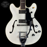 White electric guitar with a black pickguard on a black background, featuring the Guild logo.