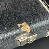 Close-up of a black pebbled leather clutch or handbag with a silver metal clasp, showing significant wear and tear with the torn leather exposing tan inner lining.