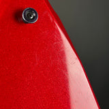 Close-up of a red metallic surface with a small dark screw or fastener near the top left and a dark gray background.