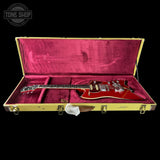 Red electric guitar in a gold case with 'Tone Shop' logo.