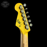 Close-up of the headstock of an electric guitar, showing a bright yellow finish on the upper portion and a natural wood tone on the lower portion, with six silver tuning pegs and a black signature on the back of the headstock. A Tone Shop watermark is visible in the top left corner.