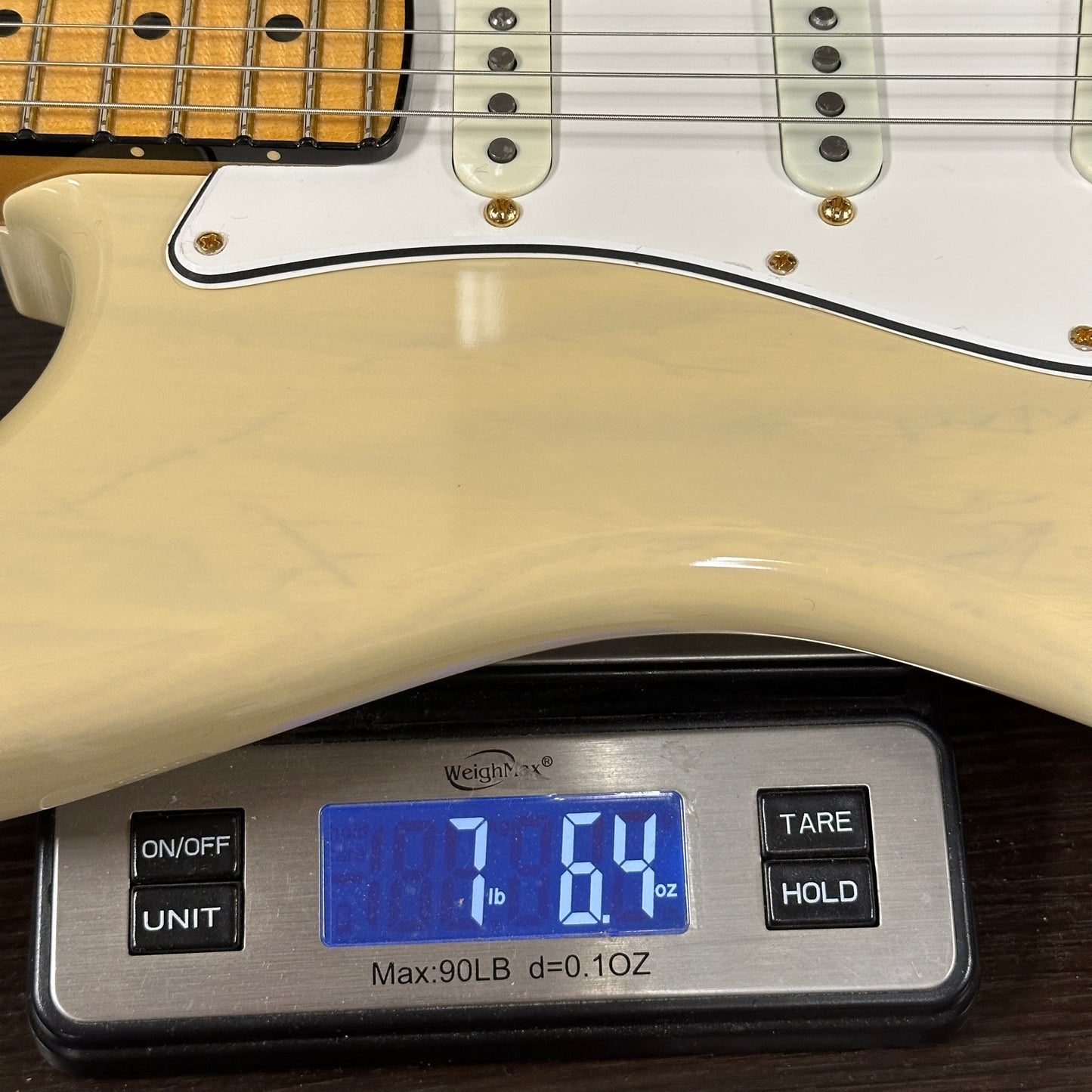 Guitar being weighed on a digital scale with a display showing weight.