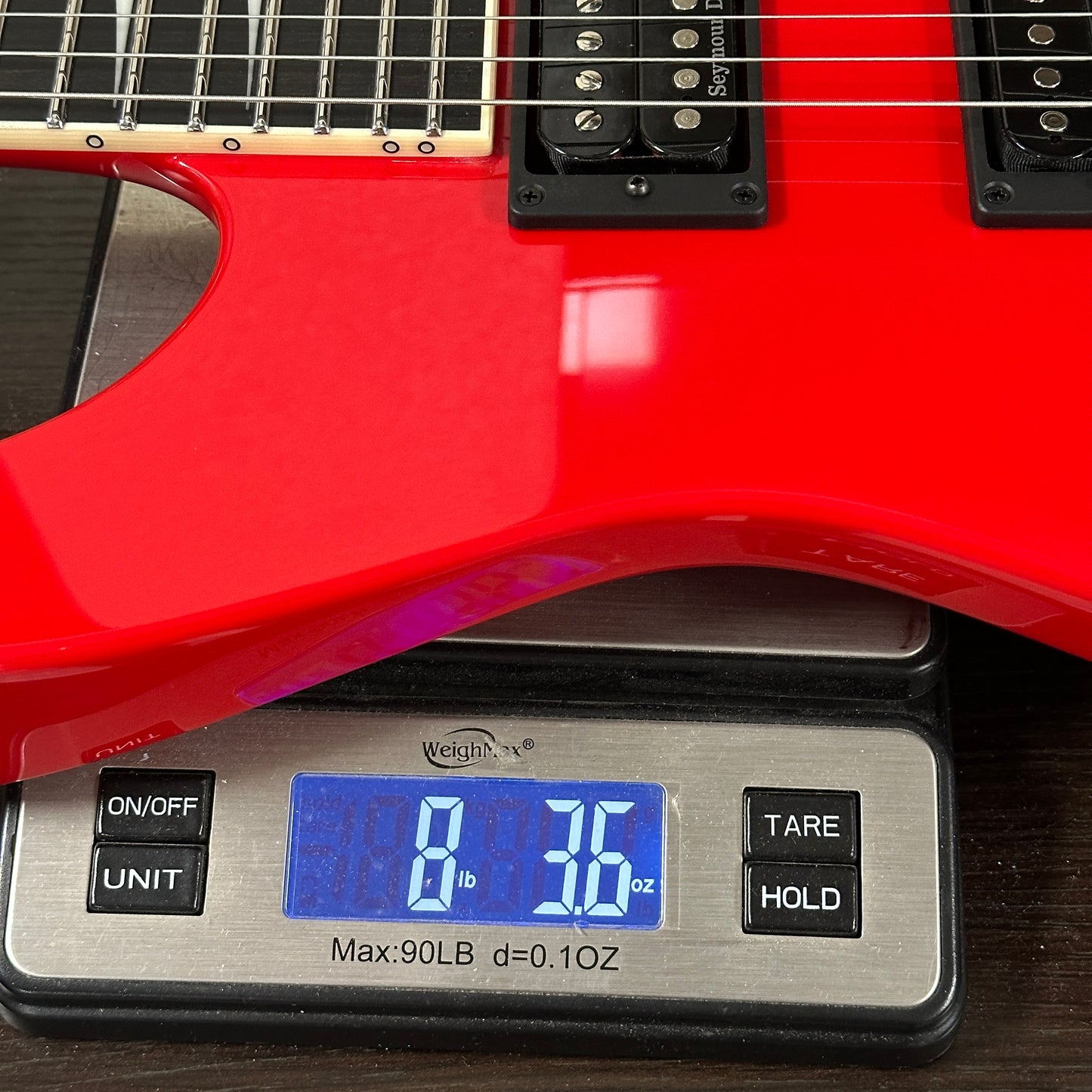 Red electric guitar on a digital scale displaying weight