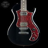 A black electric guitar with a red glittery pickguard and white binding, shown against a black background with a Tone Shop watermark in the top left corner.