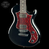 A black electric guitar with a red glitter-style pickguard, shown against a black background. A Tone Shop watermark is visible in the top left corner.