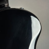 Close-up of the glossy black body of an electric guitar, showing a high-shine reflective finish and a small silver control knob against a light gray background.