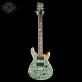 A double-cutaway electric guitar with a textured, marbled light blue-green body, dark brown maple neck, and black hardware, shown against a solid black background. A 'TONE SHOP' watermark is visible in the top-left corner.
