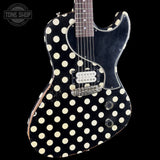 A classic electric guitar with a black body covered in large cream polka dots, featuring a black pickguard and chrome hardware, shown against a solid black background.