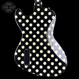 A close-up of a black electric guitar body featuring a distressed cream-colored polka dot pattern, shown against a solid black background with a Tone Shop watermark in the upper left corner.