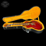 Red electric guitar in an open black and yellow case with 'Tone Shop' logo.