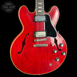 Red electric guitar with a black pickguard on a black background, featuring the Tone Shop logo.