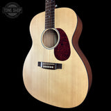 An acoustic guitar with a natural wood finish and a dark red pickguard, shown against a solid black background with a Tone Shop watermark in the top left corner.