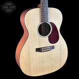 An acoustic guitar with a natural wood top, reddish-brown sides, and a dark red pickguard, shown against a solid black background with a Tone Shop watermark in the top-left corner.