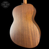Close-up of the back of an acoustic guitar showing a rich, warm brown wood grain finish against a solid black background, with a Tone Shop watermark in the upper left corner.