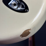 Close-up of a cream-colored guitar body with a noticeable chip and scuff on the lower portion, next to a chrome and black control plate.