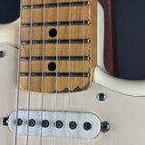 Close-up of a guitar's neck and body showing a natural wood fretboard, silver metal strings, and a cream-colored plastic pickguard.