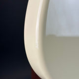 Close-up of a glossy cream-colored curved surface, likely part of a toilet bowl or similar ceramic fixture, with a dark background visible on the left.