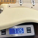 Close-up of a cream-colored electric guitar body resting on a digital scale displaying 7.126 oz.
