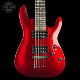 A red electric guitar with a glossy red finish, black pickups, and a dark fretboard, shown against a black background with a Tone Shop logo in the top left corner.