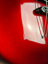 Close-up of a glossy red electric guitar body with part of the bridge and strings visible.