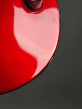 Close-up of a glossy red guitar body with a visible tuning peg and a dark gray background.