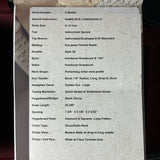 A close-up of a white product specification sheet with printed text listing details such as serial number, body size, materials, and construction for a bow. The sheet is photographed against a dark wooden surface.