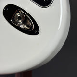 Close-up of a white guitar with a black pickguard on a dark background