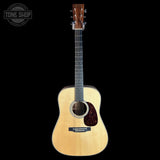 An acoustic guitar with a natural wood body, dark fretboard, and dark pickguard, shown against a solid black background with a Tone Shop logo in the top-left corner.