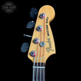 Close-up of a Fender Mustang Bass headstock with six tuning pegs, four black tuning keys, and red string tuning forks against a black background.