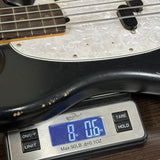 Close-up of a black and white electric bass guitar resting on a digital scale showing 8 lbs 0.5 oz, on a dark wooden surface.