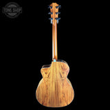 The back of an acoustic-electric guitar with a rich wood grain finish, shown against a solid black background with a Tone Shop watermark in the top left corner.