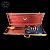 A blue electric guitar inside an open vintage wooden hard case with red velvet lining, photographed against a solid black background. A Tone Shop watermark is visible in the top-left corner.