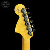 Close-up of the headstock of a yellow electric guitar against a black background, showing six silver tuning pegs and a Tone Shop watermark in the upper left corner.