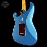 A blue electric guitar body with a yellow maple neck, shown from the back against a black background. The body has a distressed finish with a dark red pickguard and a visible scuff on the upper bout.