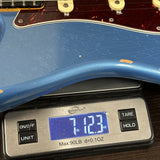 A blue electric guitar body resting on a digital scale showing a weight of 7.123 oz.