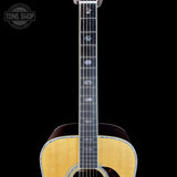 Acoustic guitar with a clear neck on a black background, featuring the Tone Shop logo.