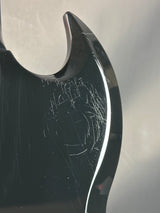 Close-up of a black guitar with visible wear and scratches on a reflective surface.