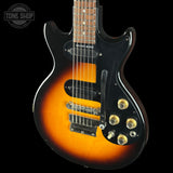 Electric guitar with sunburst finish and black pickguard on a black background, featuring 'Tone Shop' logo.